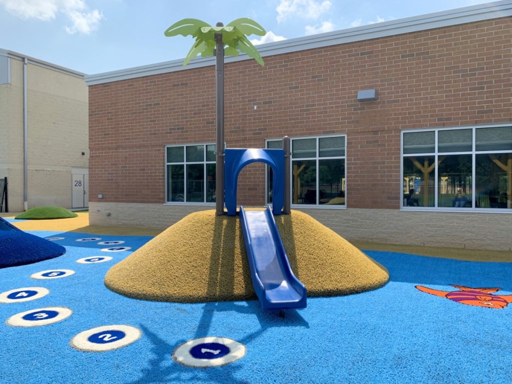 School Playground With Playground Grass In Blue With Numbered Circles, &Amp; A Fish Designed Into The Grass. Play Ground Has A Slide, Hill, &Amp; Palm Tree.